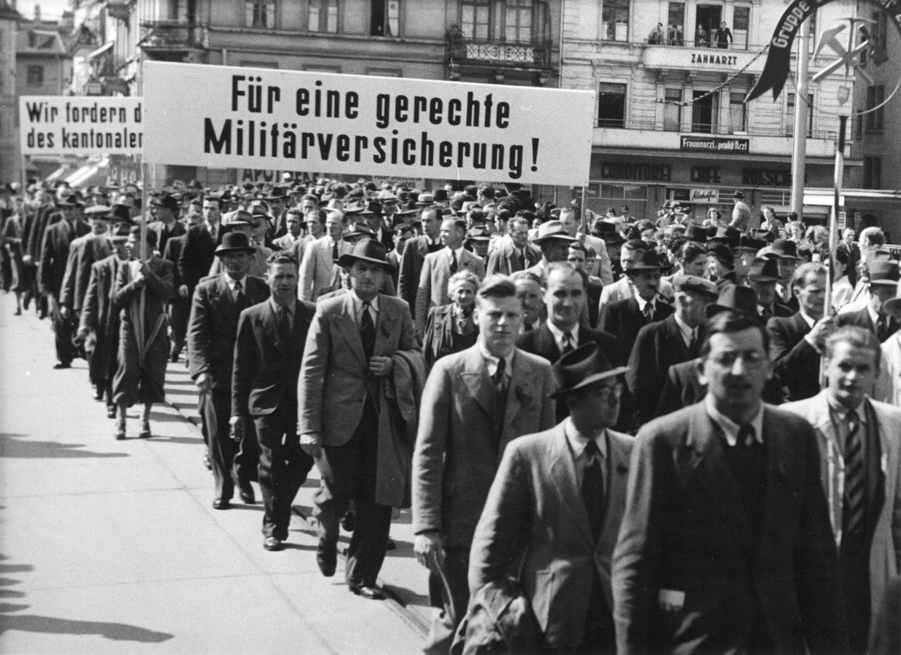 1. Mai-Umzug, Marsch mit Banner: „Für eine gerechte Militärversicherung!“. Quellennachweis: Schweizerisches Sozialarchiv, Zürich, Sozarch_F_5047-Fb-090.